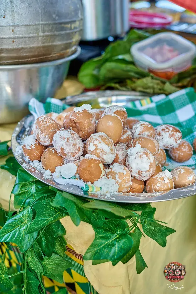A tray of salt-baked eggs on a stall table, dressed with green leaves and kente cloth