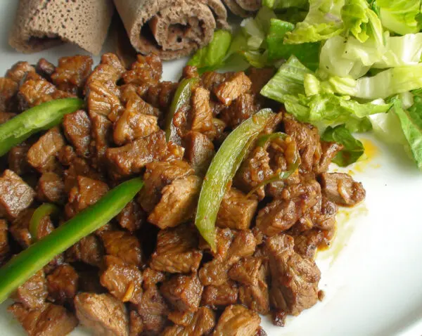 Ethiopian Tibs stir-fried beef in a clay pot with onions, rosemary, and jalap peppers served on injera