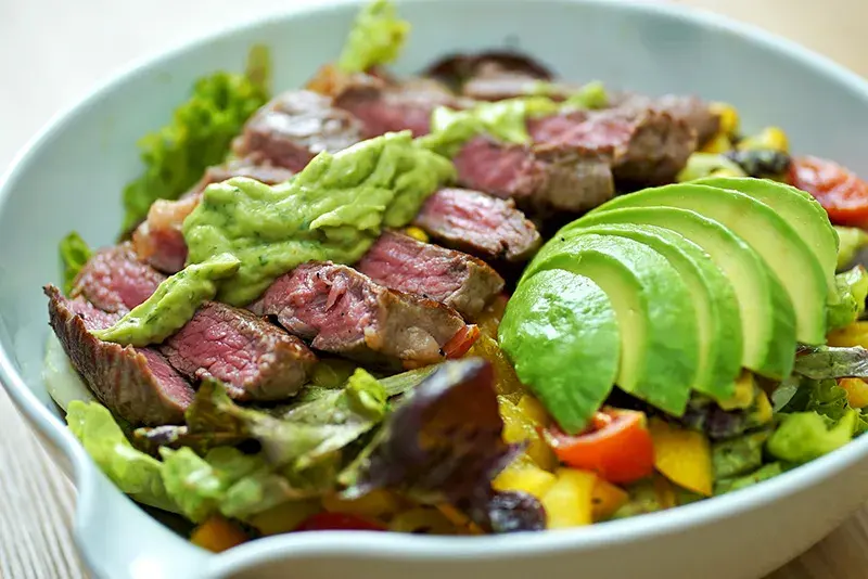 Sliced grilled steak served over diced avocado, tomato and onion salad