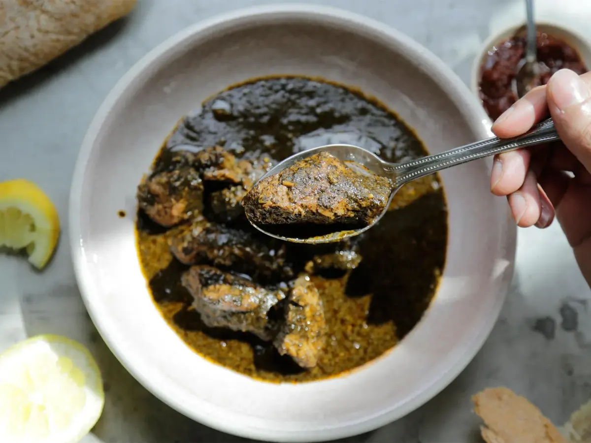 Tunisian mloukhia, a dark slow cooked stew of dried jute mallow powder with lamb, served with bread