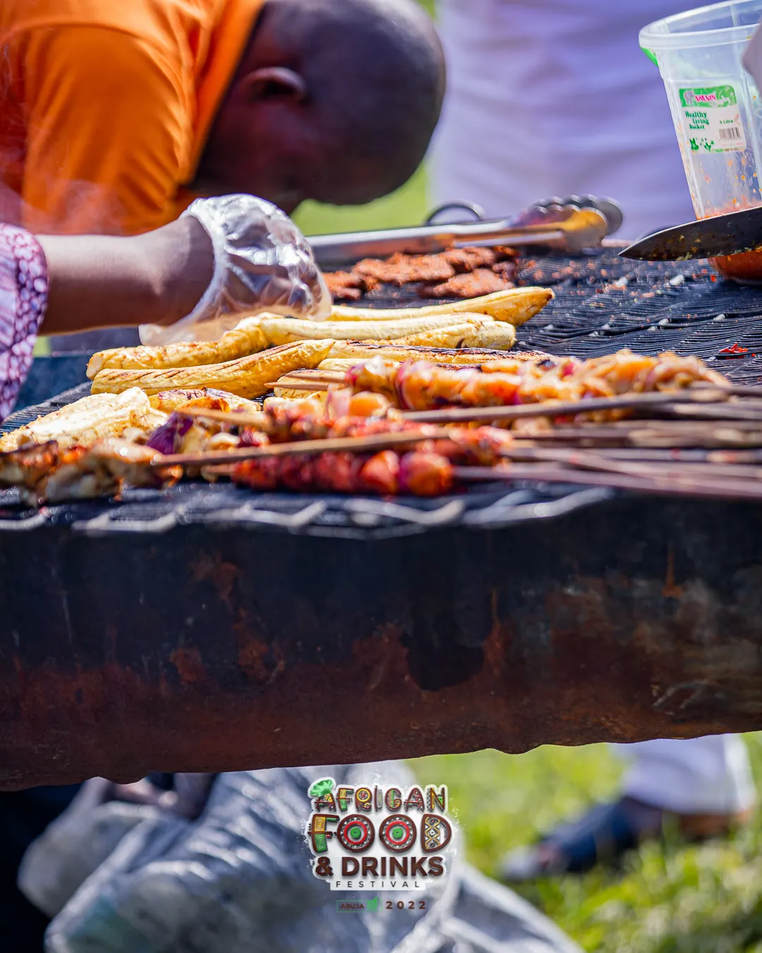 Des brochettes de suya et des kebabs alignés sur un gril ouvert, une main gantée au-dessus