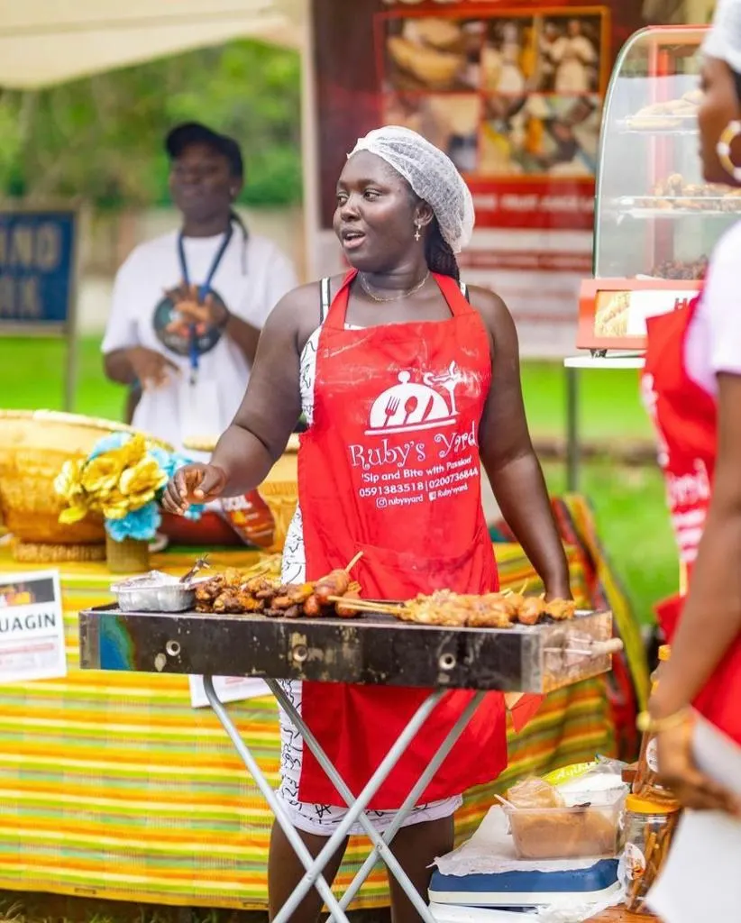 Une cuisinière en tablier rouge retourne des brochettes sur un gril à son stand