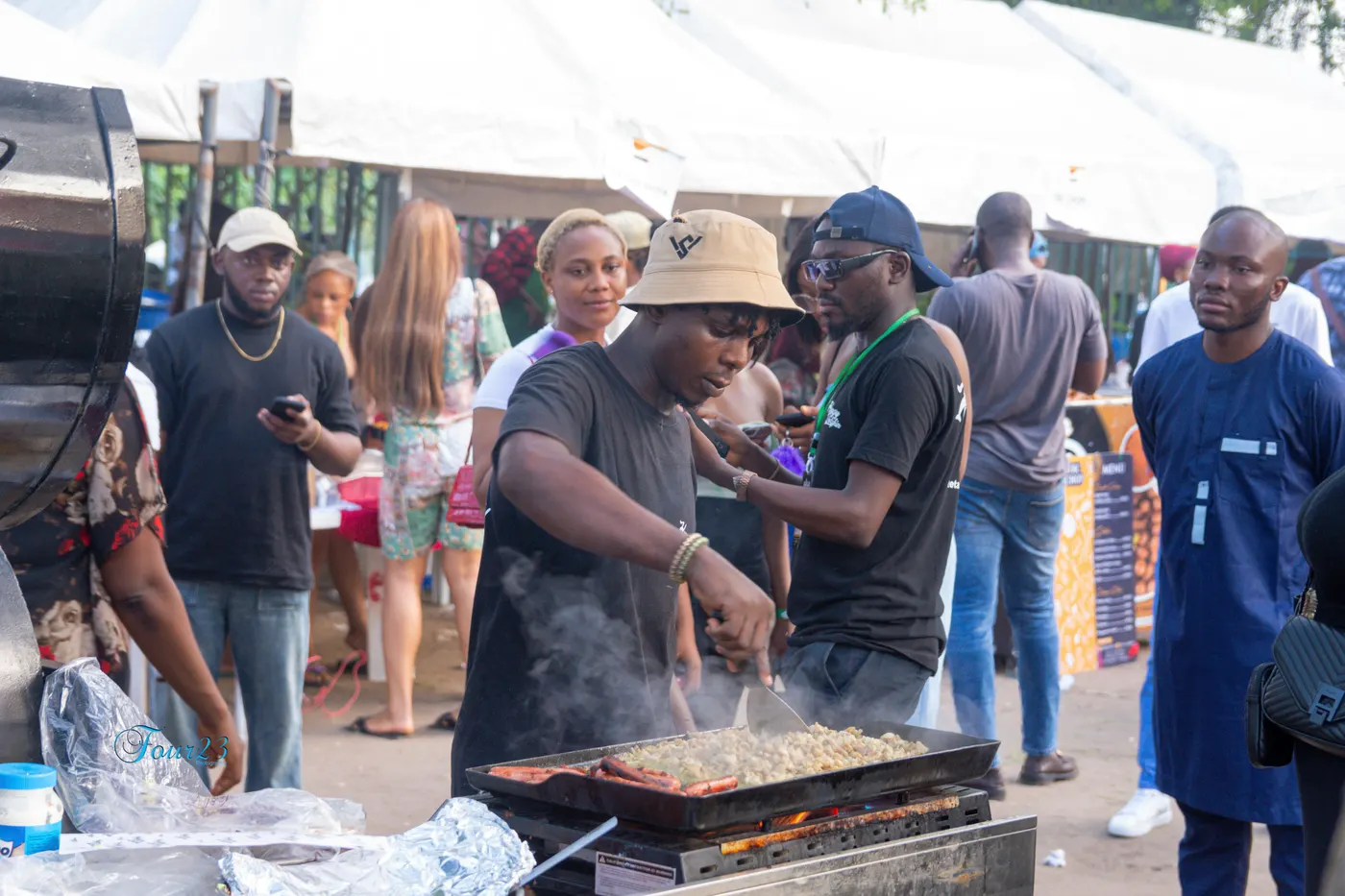 Un cuisinier s'affaire sur une plancha fumante à son stand pendant que les invités attendent autour de lui