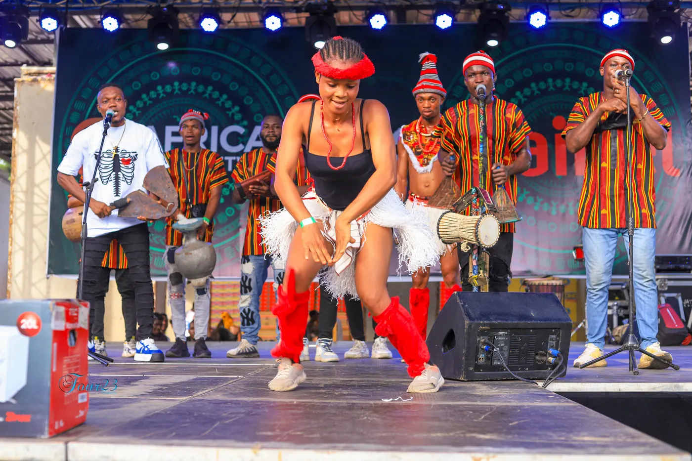 Une danseuse en bottes rouges et bandeau rouge sur scène avec quatre percussionnistes en tissu rayé