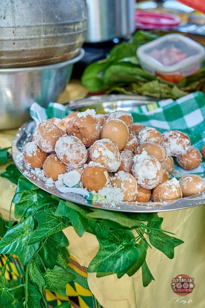 Un plateau d'œufs cuits au sel sur la table d'un stand, garni de feuilles vertes et de tissu kente