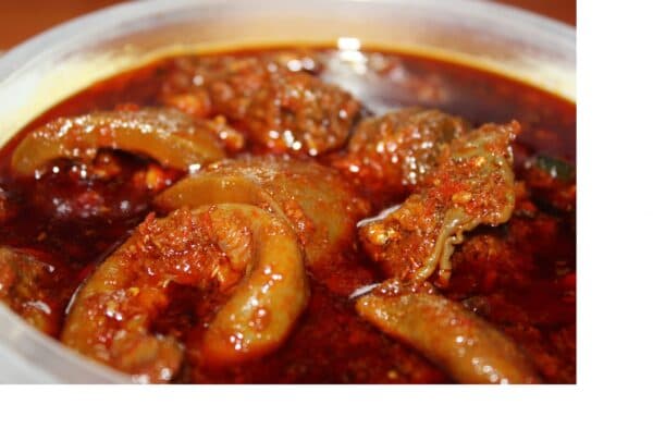Ofada Stew Nigerian red bell pepper sauce with assorted meat and boiled eggs in a pot, served with Ofada rice on banana leaves