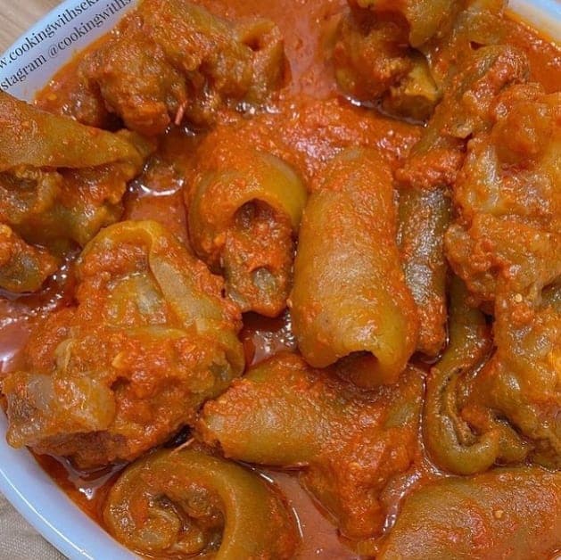 Nigerian Peppered Cow Leg Bokoto pieces in a spicy pepper sauce in a pan, a popular Lagos street food and party snack