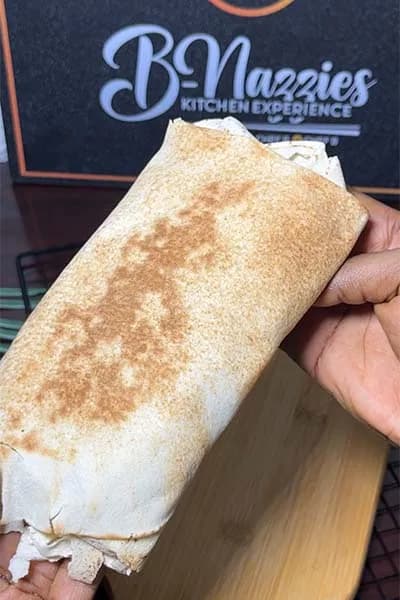 Nigerian cheese shawarma, a flatbread wrap filled with fried protein, sausage, slaw and melted mozzarella