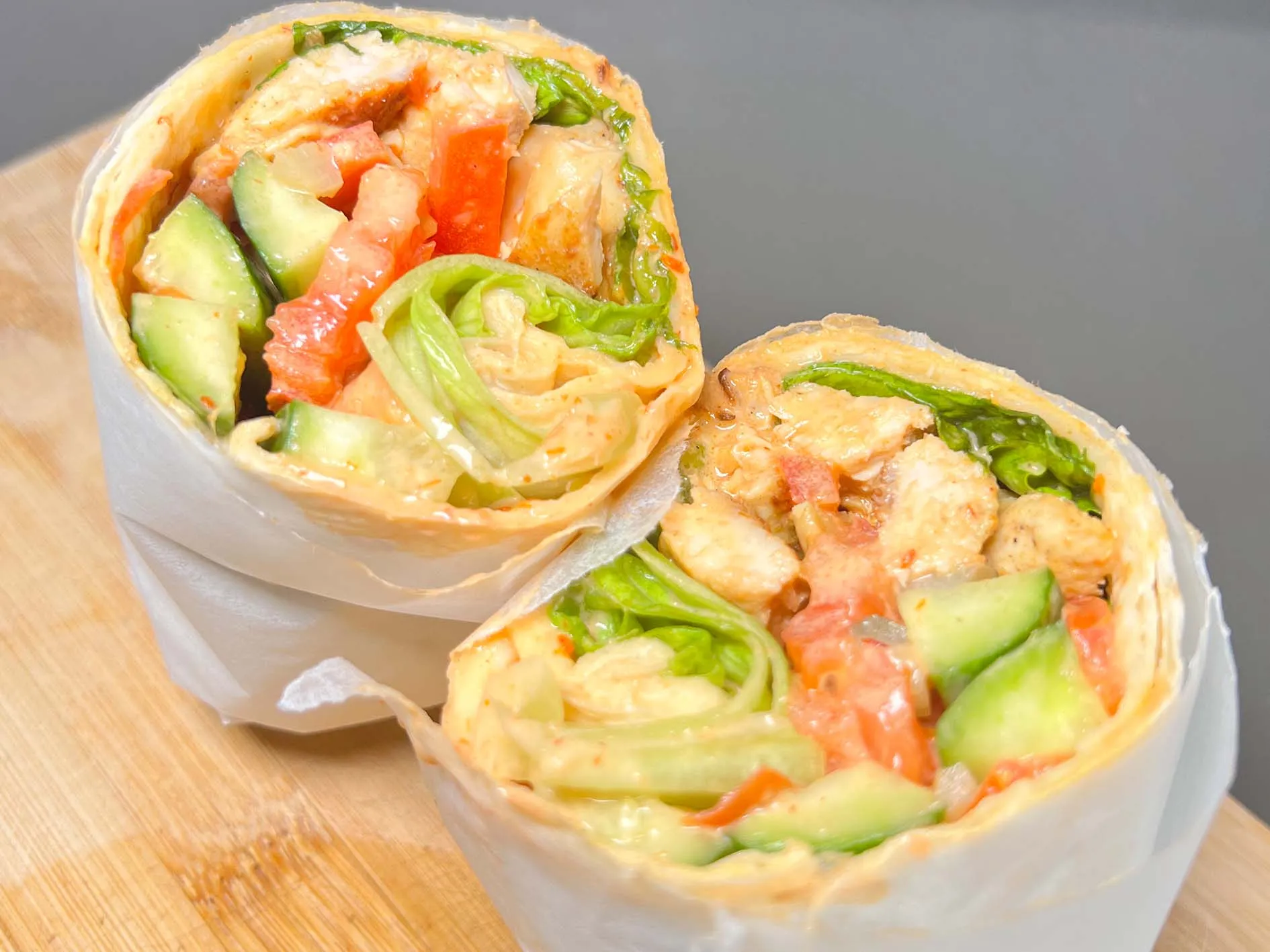 A chicken wrap with salad and sauce, toasted and cut in half