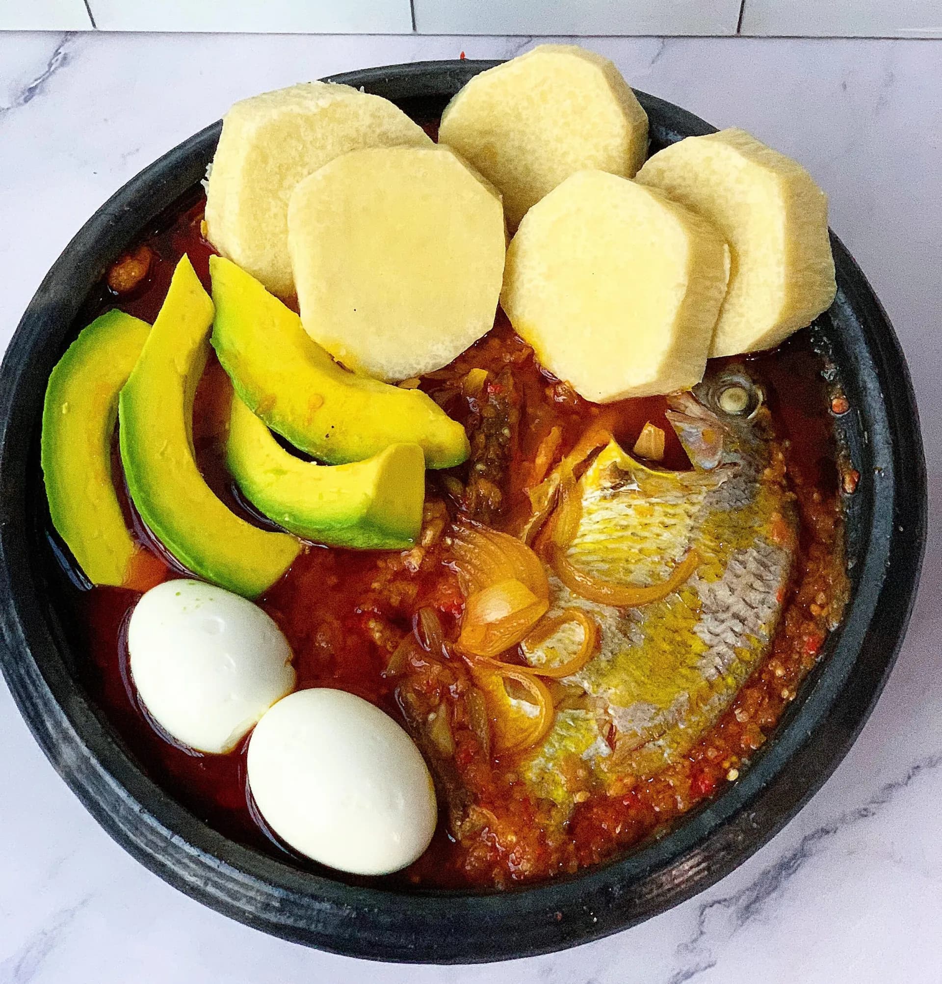 Garden Egg Stew, a Ghanaian stew ground in an earthenware bowl and served with boiled yam and avocado