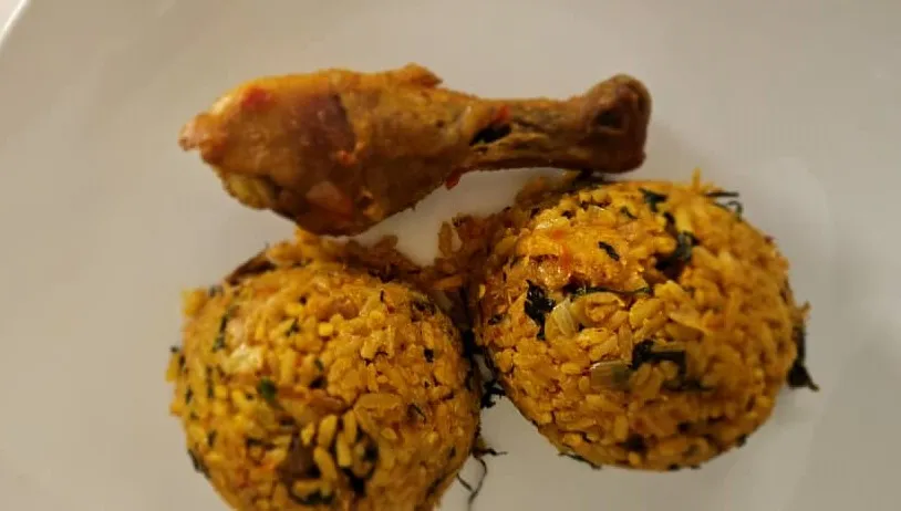 Nigerian native jollof rice, palm oil rice with locust beans, smoked fish and scent leaf